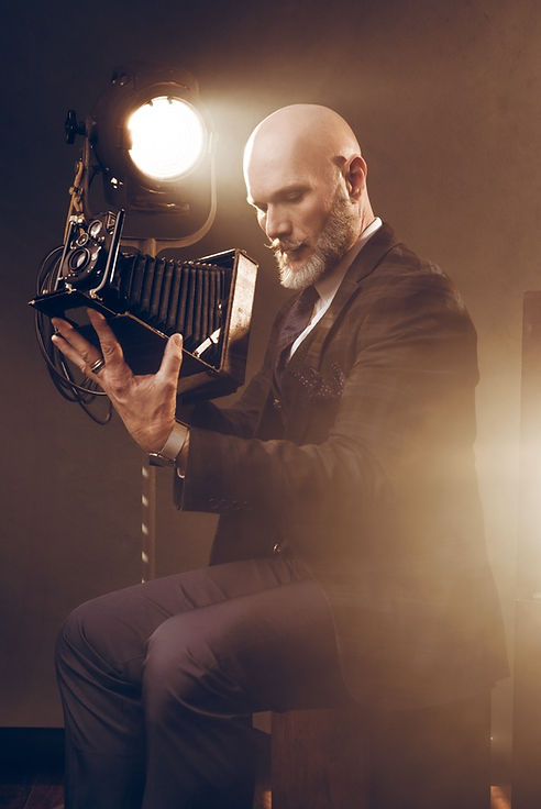 Bald man in suit examines vintage camera, Jordan Licon Photography