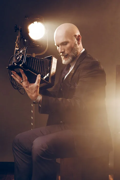 Bald man in suit examines vintage camera, Jordan Licon Photography